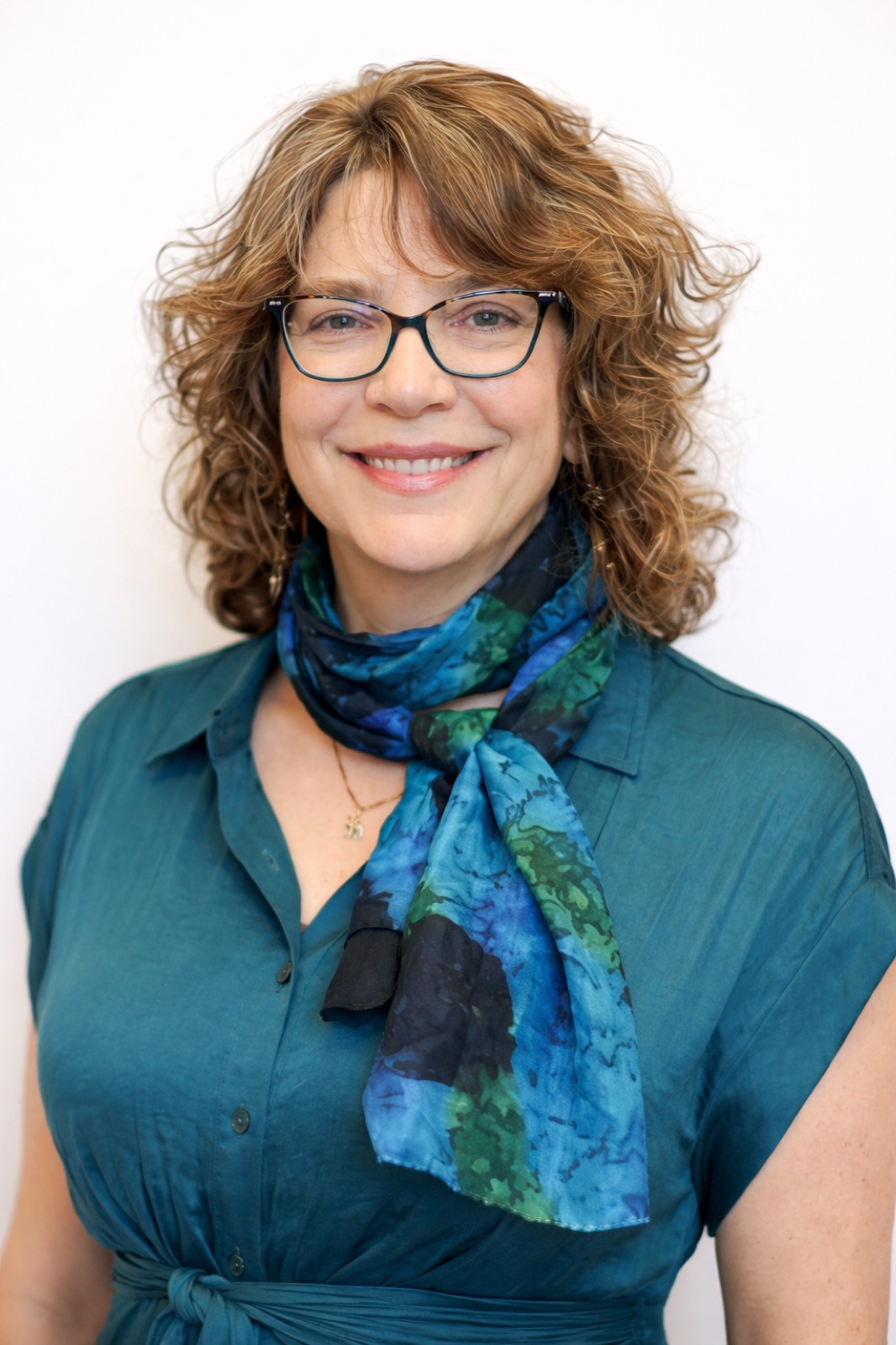 Portrait of Carol Chase, smiling warmly, wearing a teal blouse and a blue-and-green scarf.